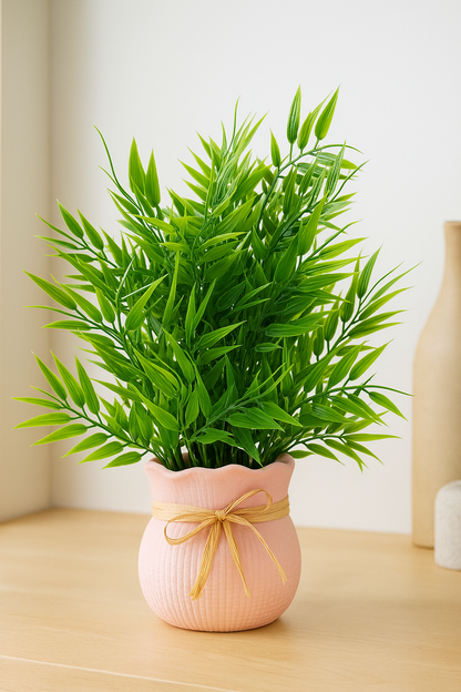Green potted plant in a pink pot with a yellow ribbon on a wooden surface.